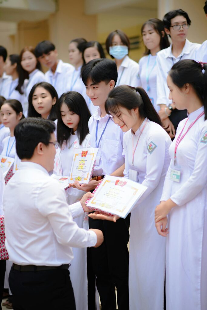Group of Asian students receiving certificates during a graduation ceremony indoors.