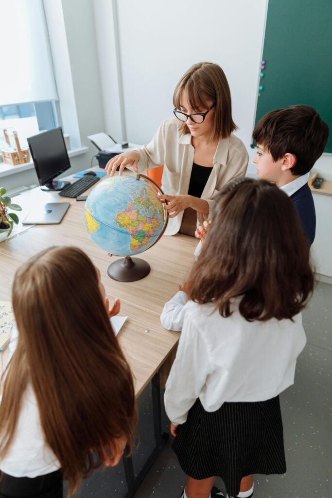 Students learning geography with teacher using a globe in a bright classroom setting.